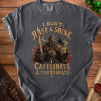 Dark gray t-shirt with knight holding sword and coffee mug, text reads "I DON'T RISE & SHINE. I CAFFEINATE & COORDINATE."