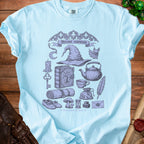 Light blue t-shirt with "Hermit essentials" text and gothic illustrations of witchy items.