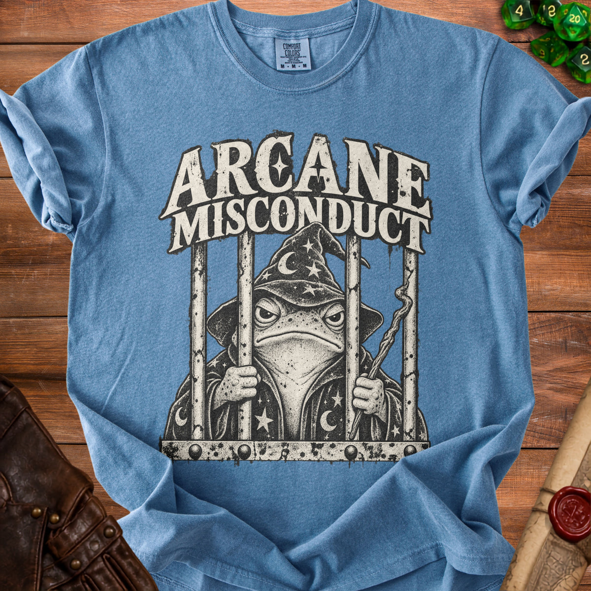 Blue t-shirt with a frog wizard in jail and the text "Arcane Misconduct".