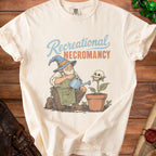 Cream t-shirt with graphic of wizard watering a skull plant, text "Recreational Necromancy."