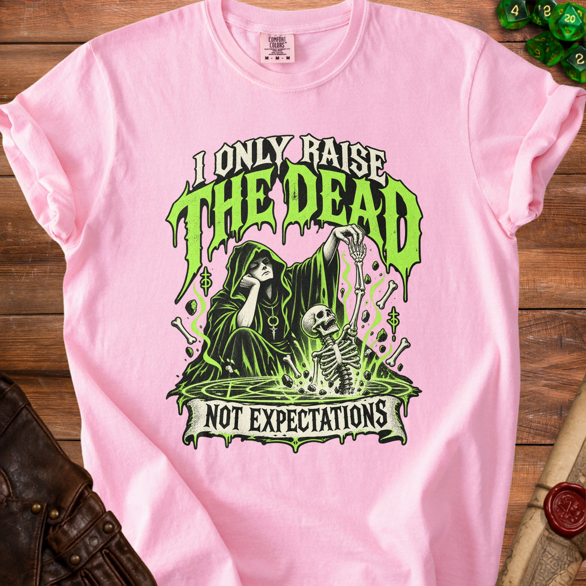 Pink t-shirt with grim reaper and skeleton graphic reading "I Only Raise the Dead Not Expectations."