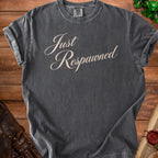 Dark gray t-shirt with "Just Respawned" in cursive on a wooden background.