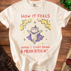 Cream t-shirt with cat in wizard hat and text "How it feels when I start being a mean bitch again."