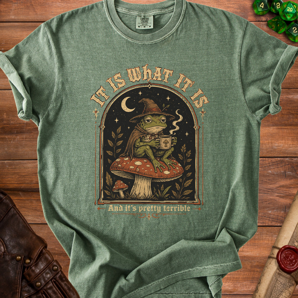 Green t-shirt with a frog wearing a witch hat holding coffee and text "IT IS WHAT IT IS And it's pretty terrible".