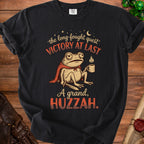 T-shirt with a frog wearing a cape, holding a mug, and text "VICTORY AT LAST" and "A grand, HUZZAH."