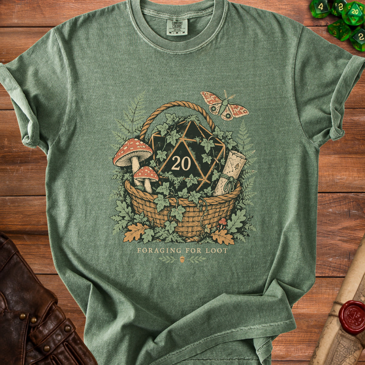 Green t-shirt graphic with d20 dice, basket, mushrooms, scroll, and moth.