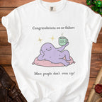 White t-shirt with cartoon: "Congratulations on ur failure. Most people don't even try!"