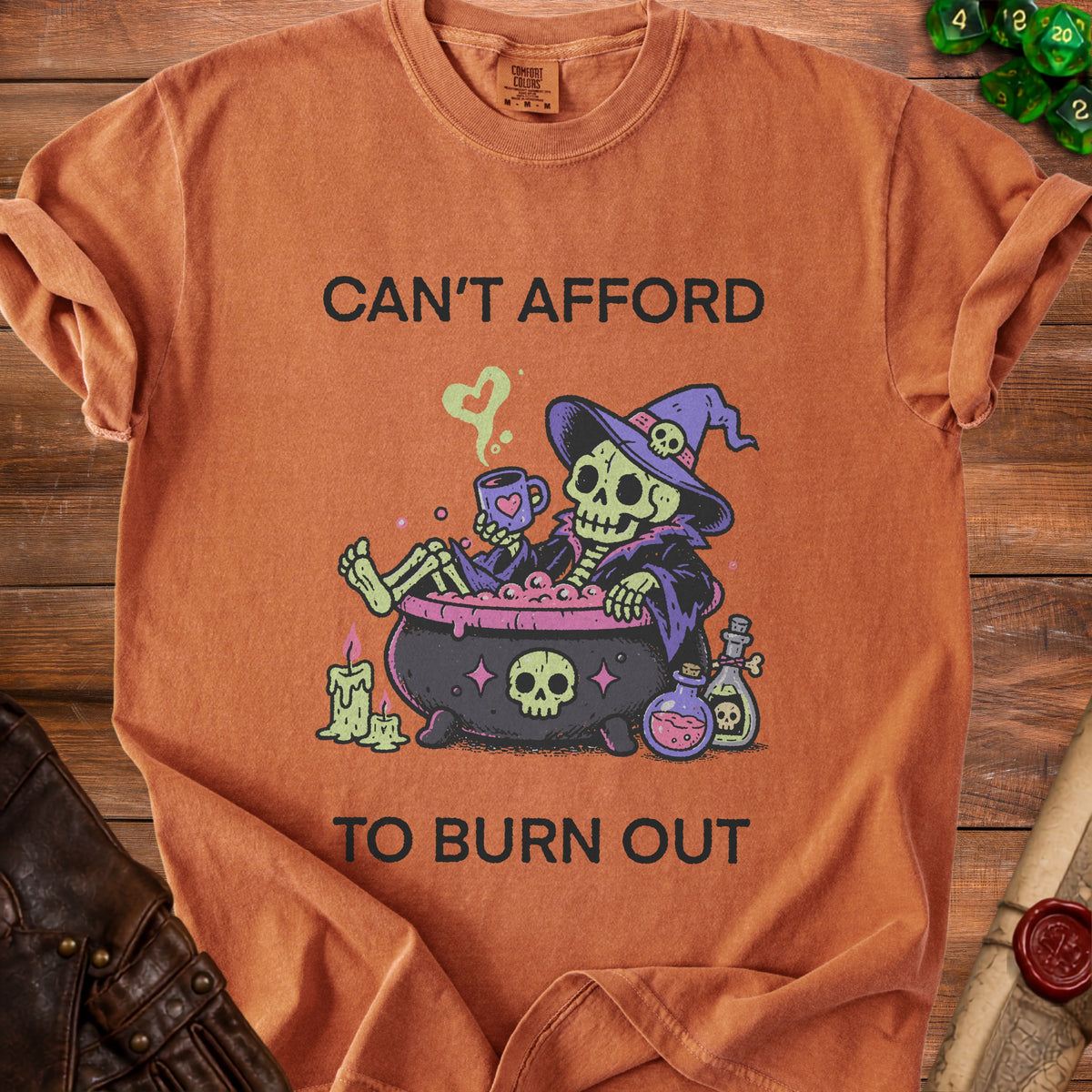 Orange t-shirt with skeleton in cauldron graphic and text "CAN'T AFFORD TO BURN OUT".