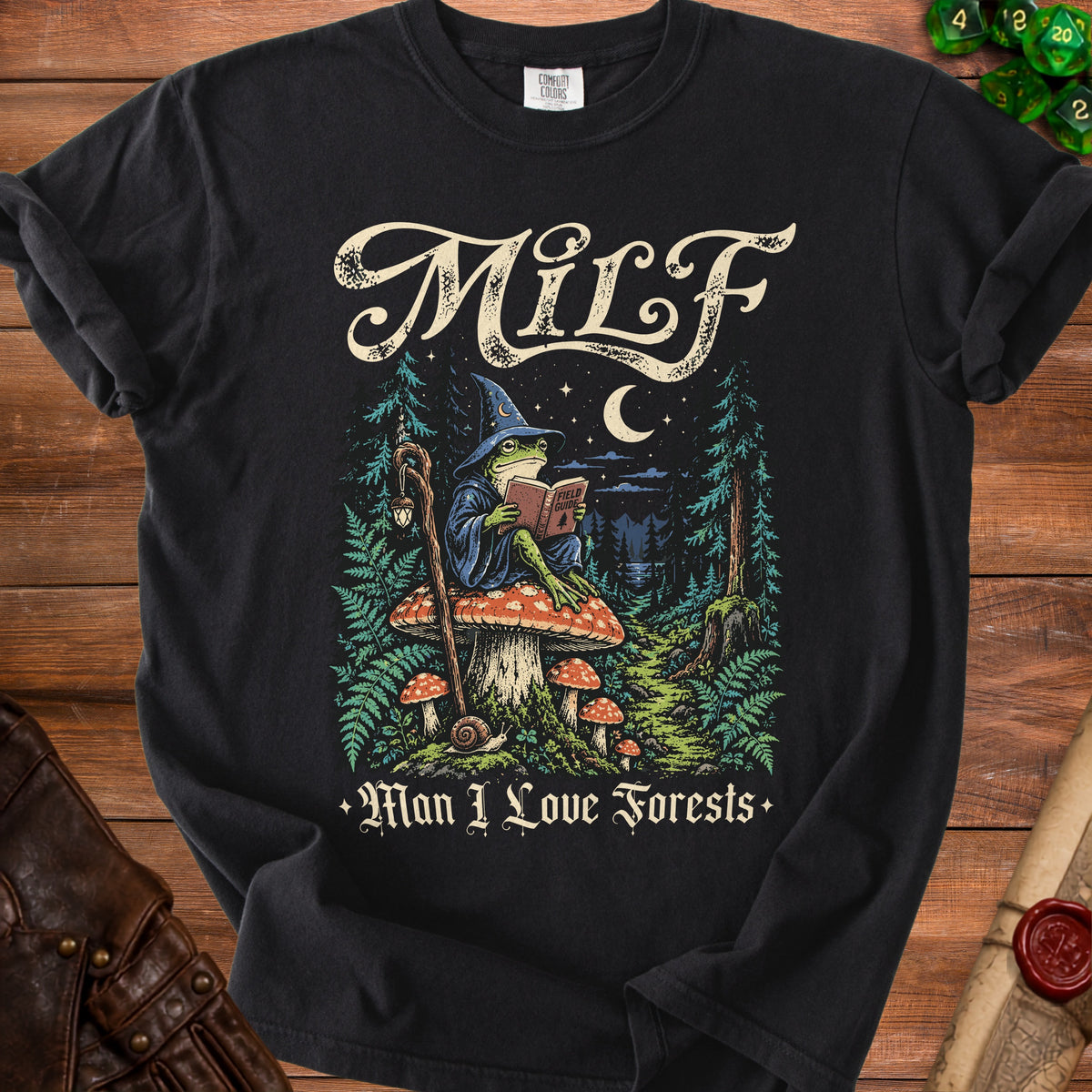 Black t-shirt with MILF and frog wizard reading a field guide in a forest.