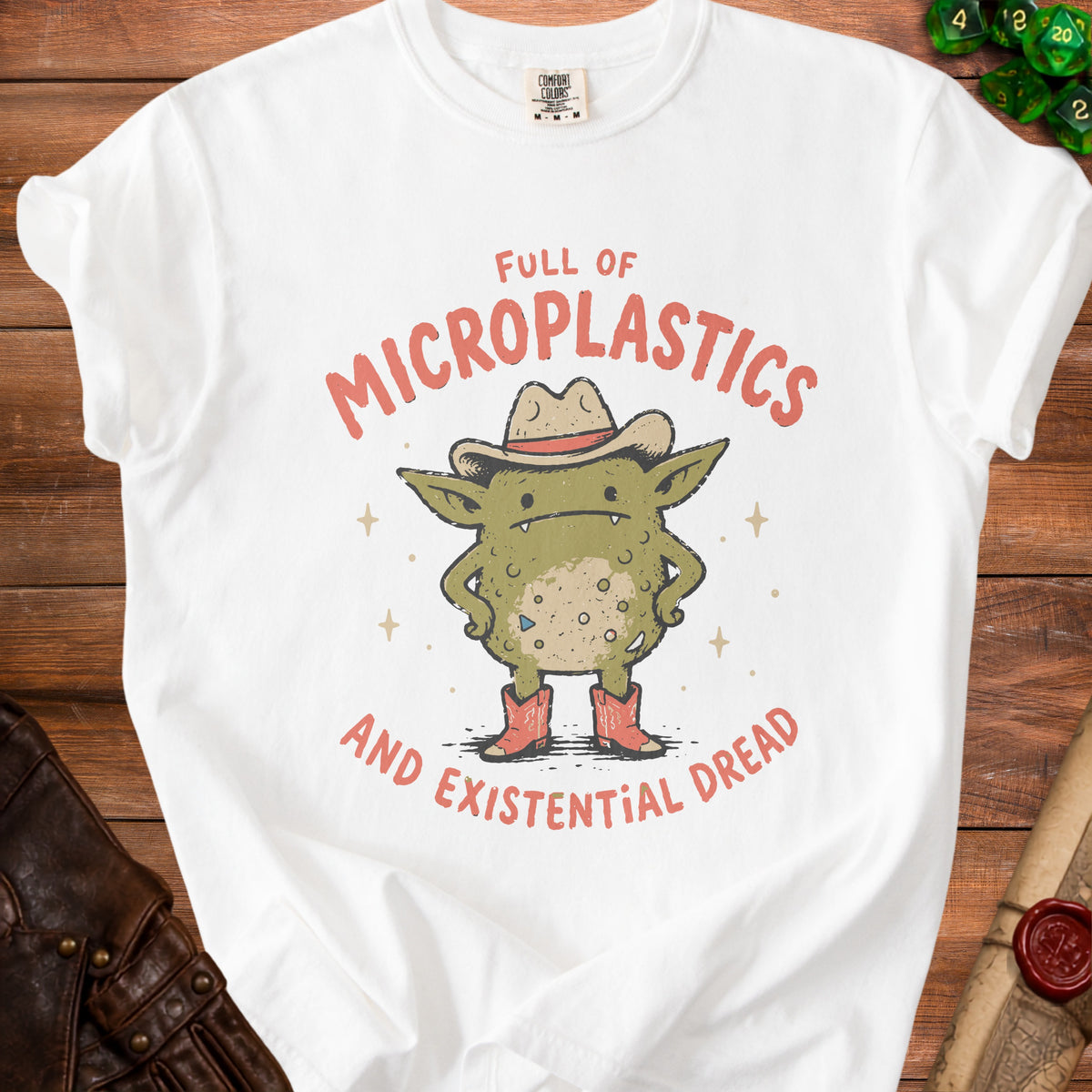 White t-shirt with a cartoon creature wearing a cowboy hat and boots, text reads "Full of Microplastics and Existential Dread."