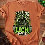 Orange t-shirt with a graphic of a hooded skeleton and "Resting Lich Face" text.