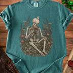 Skeleton holding a flower, surrounded by flowers and butterflies, with a Comfort Colors tag.