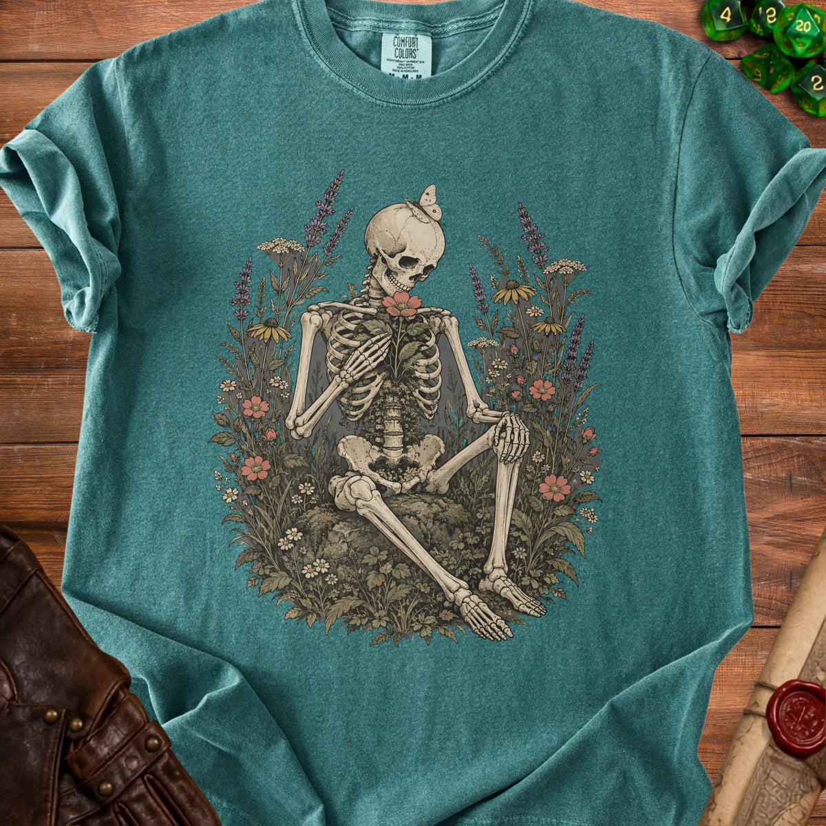 Skeleton holding a flower, surrounded by flowers and butterflies, with a Comfort Colors tag.