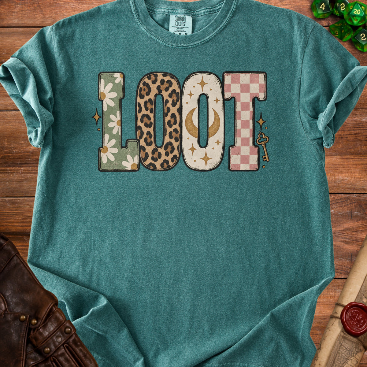 Teal t-shirt with "LOOT" graphic featuring daisies, leopard print, moon, and checkerboard patterns.