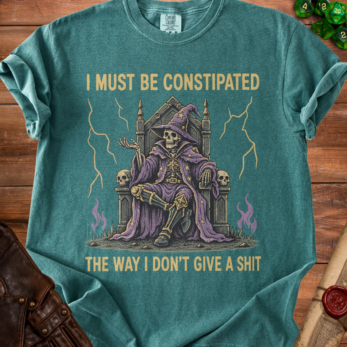 Teal t-shirt with skeleton wizard on throne and text "I must be constipated the way I don't give a shit".