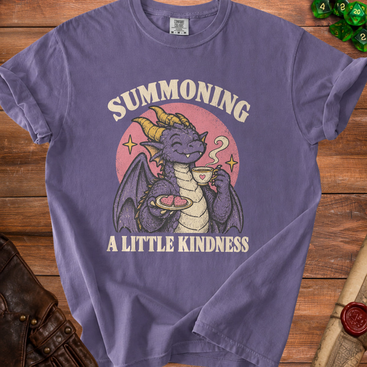 Purple t-shirt with a dragon drinking tea and holding heart cookies, text "Summoning A Little Kindness".