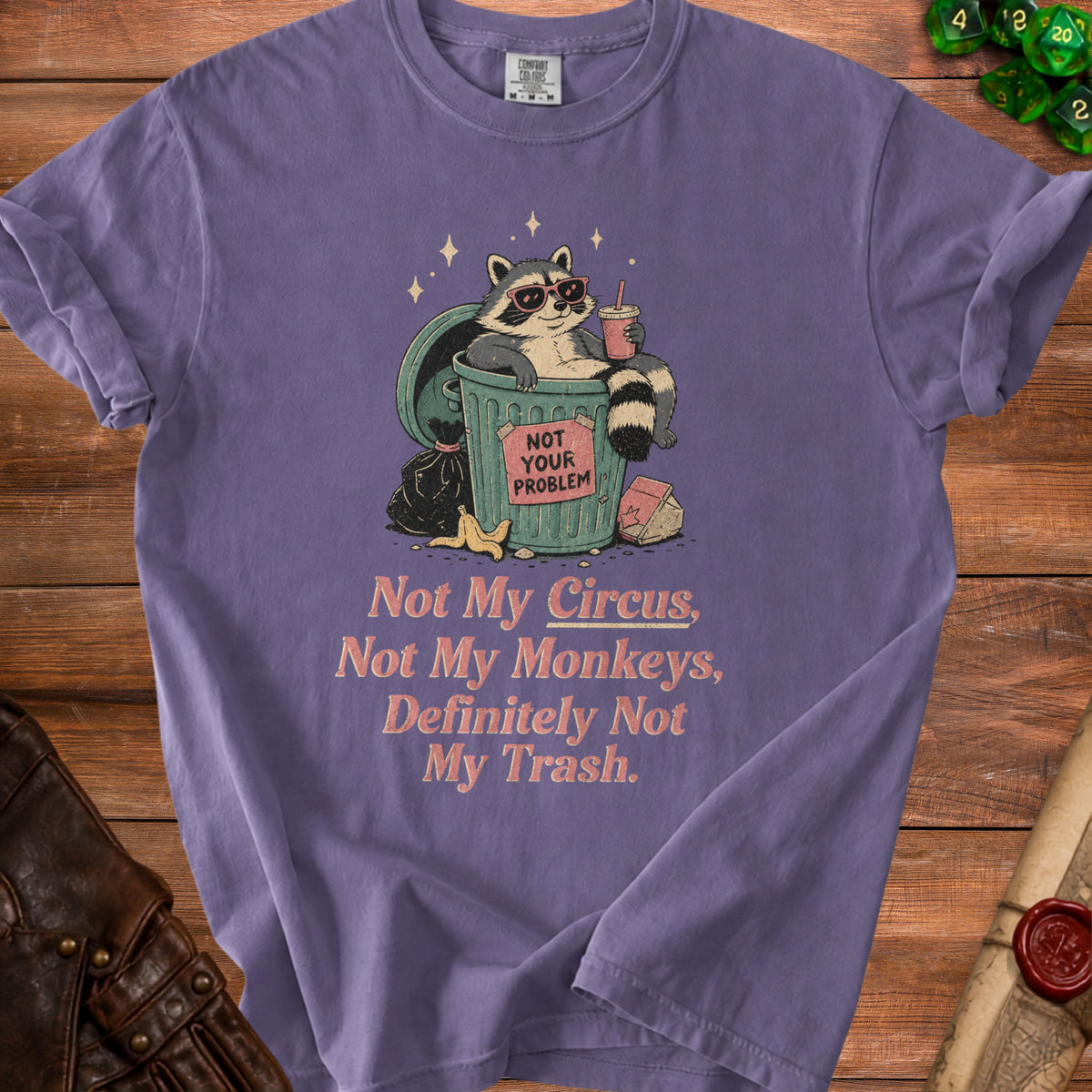 Purple t-shirt with graphic of raccoon in trash saying "Not Your Problem."