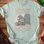 Mint green t-shirt with graphic of gnome holding "not my problem" mug, text about work.