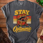 Dark grey t-shirt with "STAY Optimimic" text and a monster treasure chest graphic.