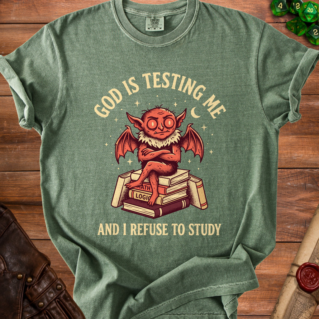 Green t-shirt with a graphic of a devil sitting on books, text reads "GOD IS TESTING ME AND I REFUSE TO STUDY".