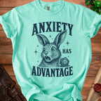 Aqua t-shirt with graphic "Anxiety Has Advantage" and scared rabbit next to d20 die.