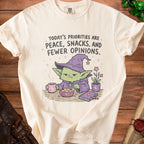 Cream t-shirt with text "Today's Priorities Are Peace, Snacks, and Fewer Opinions" and goblin graphic.