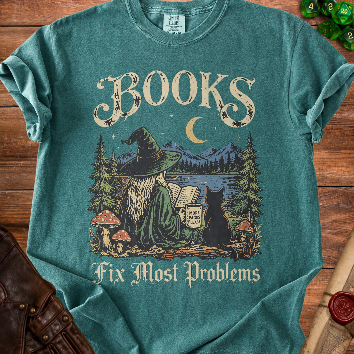 T-shirt with graphic of witch reading by a lake, black cat, moon, mountains, and text: Books Fix Most Problems.