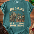 Teal t-shirt with graphic "The Garden Is Plotting Something" featuring a gnome and potted plants.
