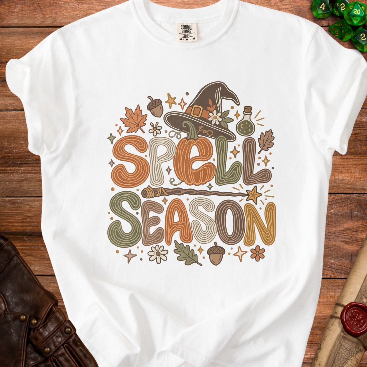 White t-shirt with "Spell Season" text, pumpkin, witch hat, and autumn leaves graphic.