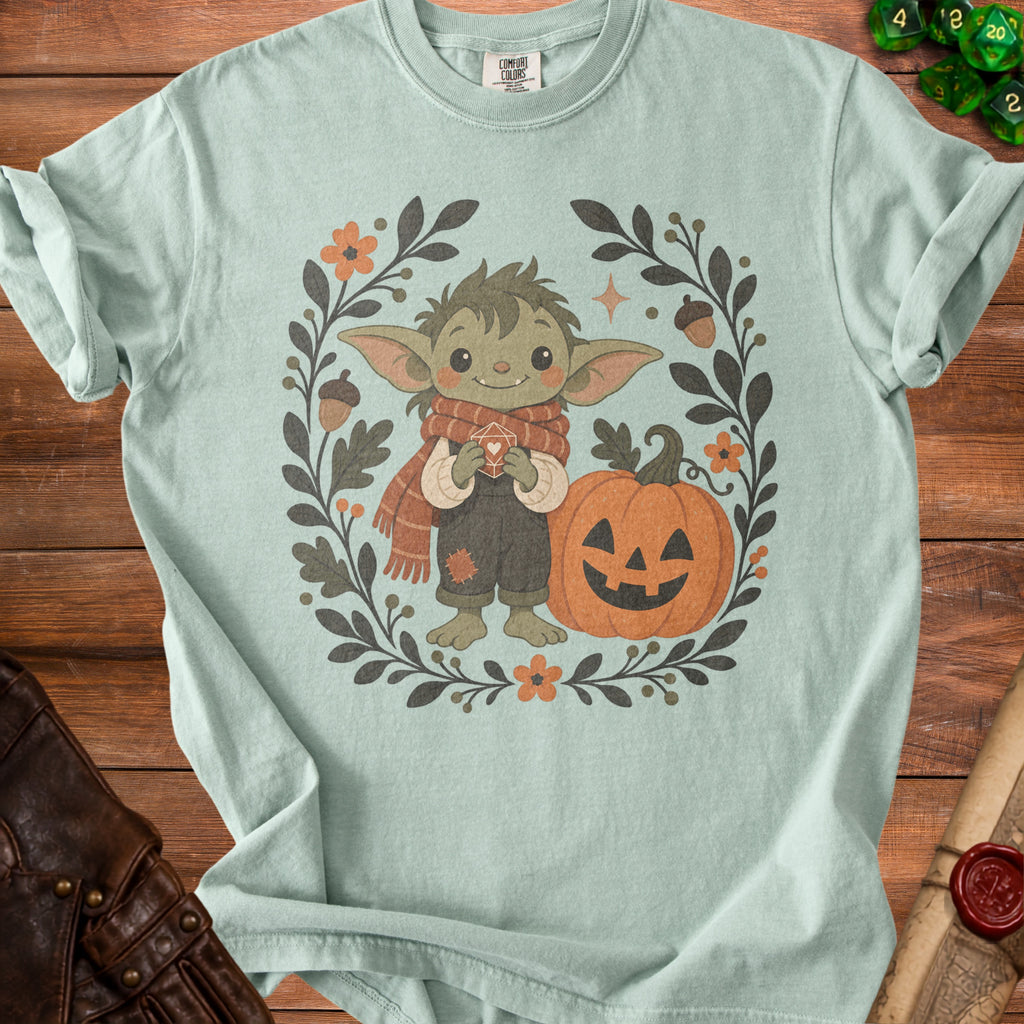 Green creature in scarf holding dice, with pumpkin and floral wreath.