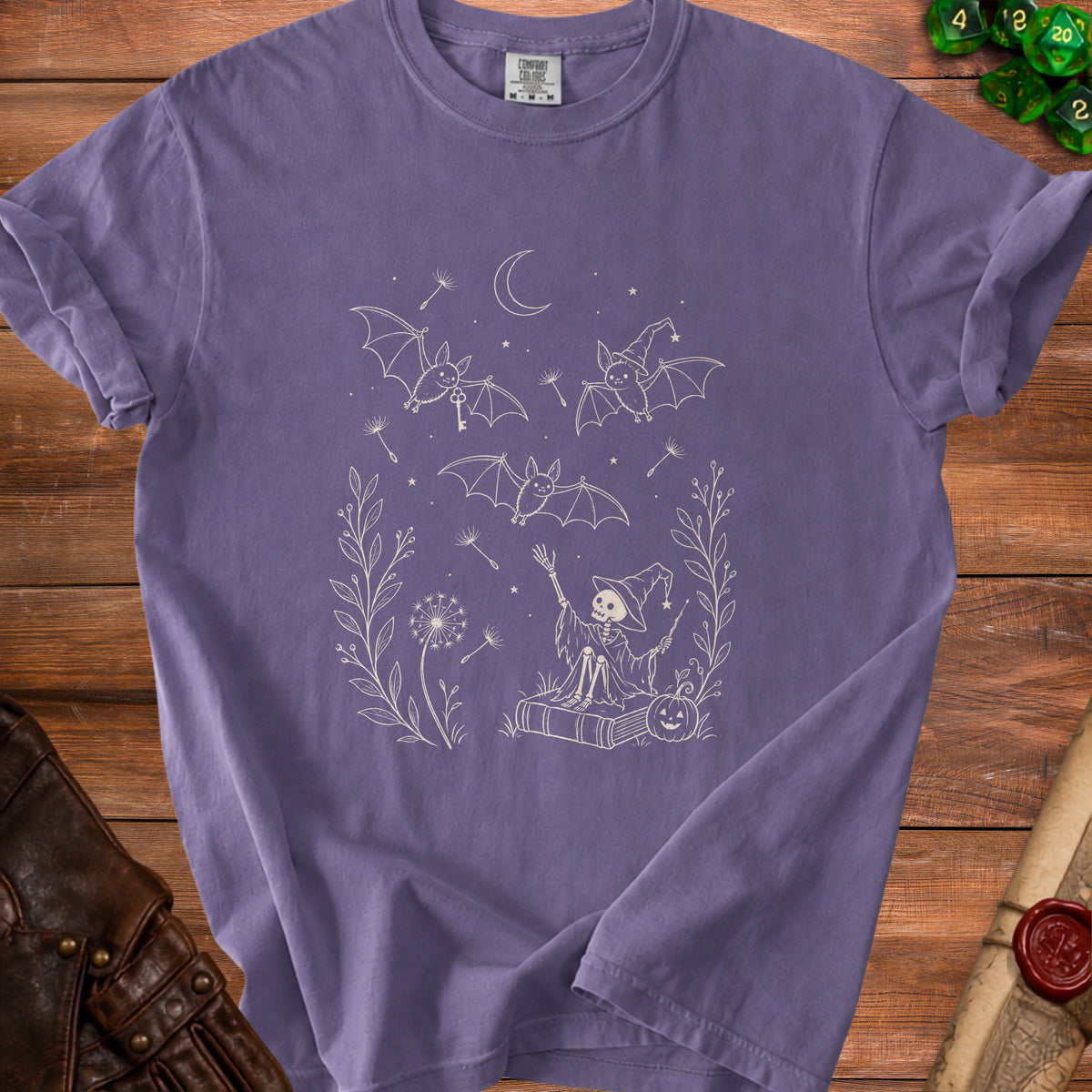 Purple t-shirt with a line drawing of a skeleton witch, bats, and dandelions.