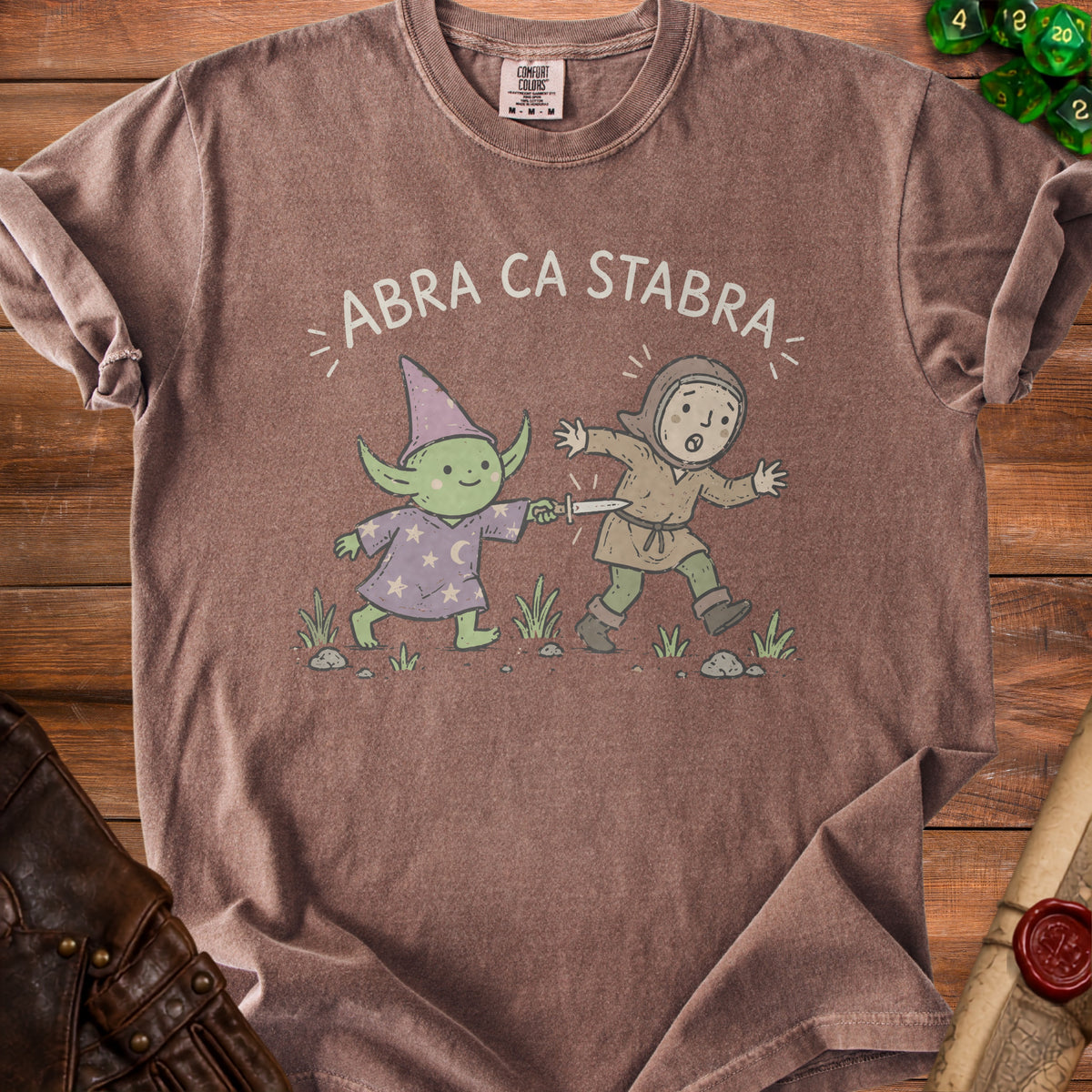 Brown t-shirt with "ABRA CA STABRA" text and cartoon wizard stabbing a character.