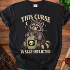 Black t-shirt graphic of a raccoon drinking from a bottle labeled with a skull. Text reads "THIS CURSE IS SELF-INFLICTED."