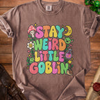 Brown t-shirt with "Stay Weird Little Goblin" text and whimsical illustrations.
