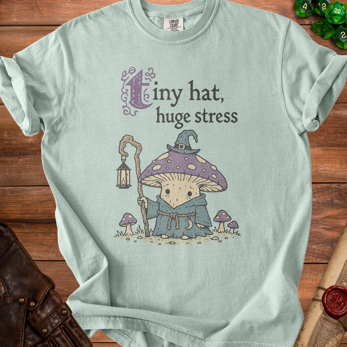 Light blue t-shirt with graphic of mushroom character and text "tiny hat, huge stress".