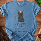 Blue t-shirt with a grumpy black cat wearing a party hat and text about 9-5 and unemployment.