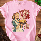 Pink t-shirt with a retro illustration of a woman holding a pie, "Shut Your Spell Hole" text.