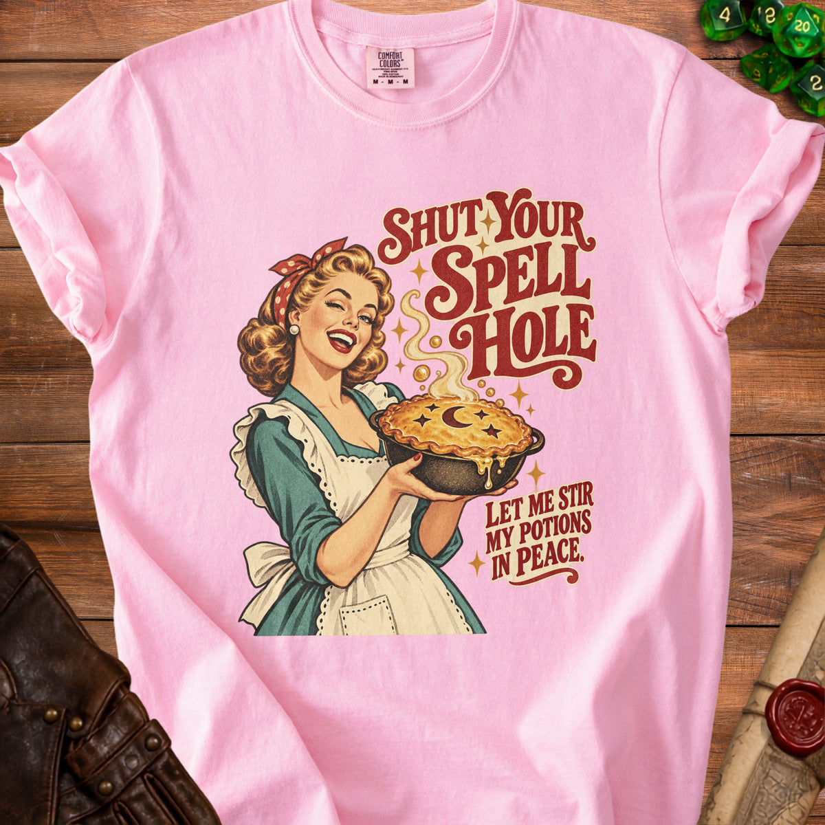 Pink t-shirt with a retro illustration of a woman holding a pie, "Shut Your Spell Hole" text.