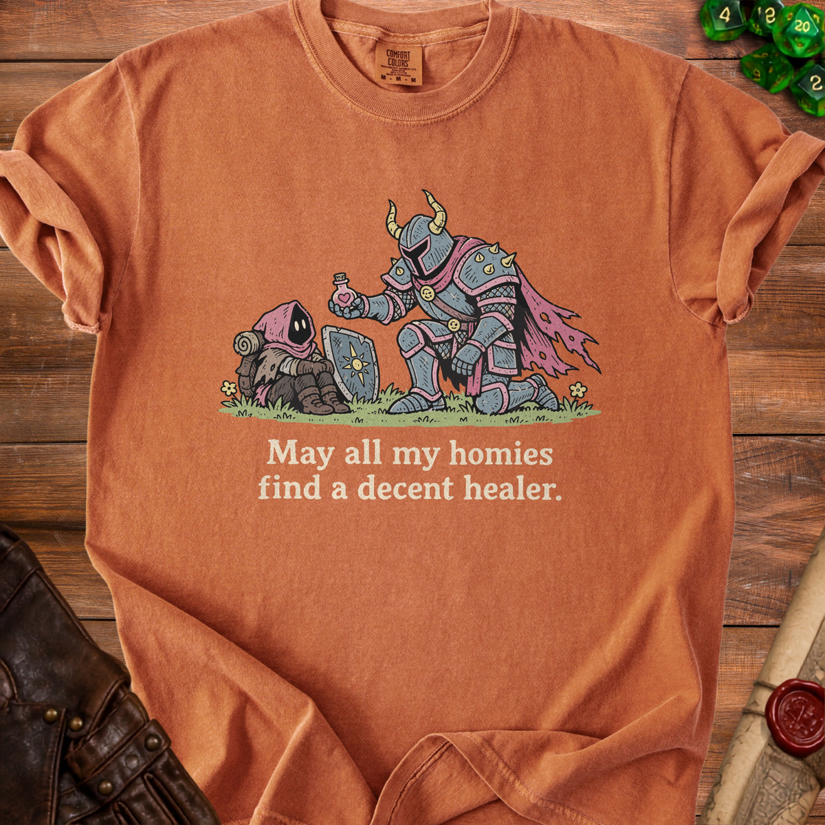 Orange t-shirt with illustration of knight giving potion to hooded figure, text "May all my homies find a decent healer."