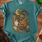 Goblin witch with pumpkin, moon, ghost, and haunted house on a teal t-shirt.