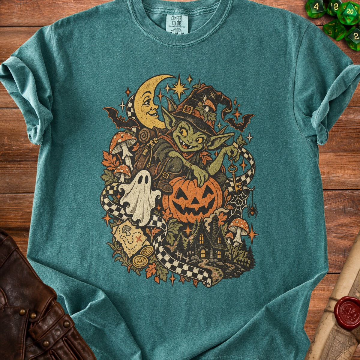 Goblin witch with pumpkin, moon, ghost, and haunted house on a teal t-shirt.