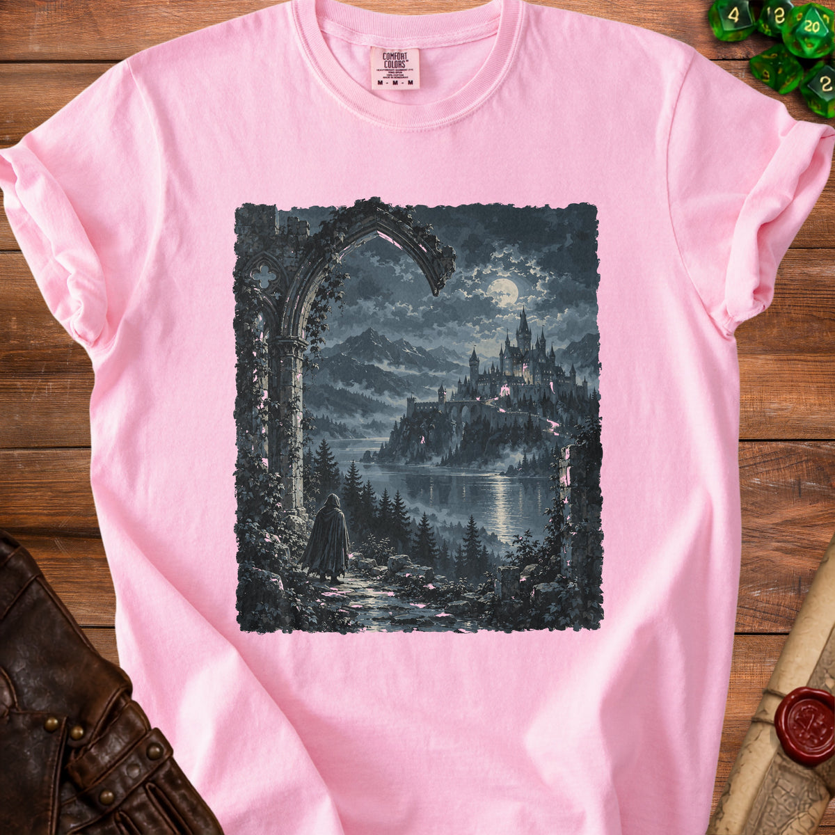 Pink t-shirt with a hooded figure walking towards a moonlit castle by a lake.