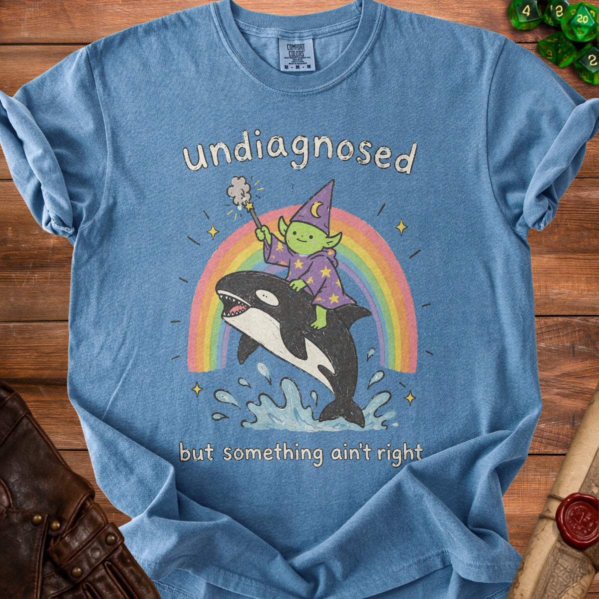 Blue t-shirt with text "undiagnosed" and a drawing of a wizard riding an orca over a rainbow.