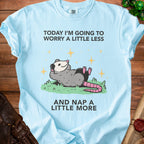 Light blue t-shirt with a possum graphic and text "TODAY I'M GOING TO WORRY A LITTLE LESS AND NAP A LITTLE MORE".