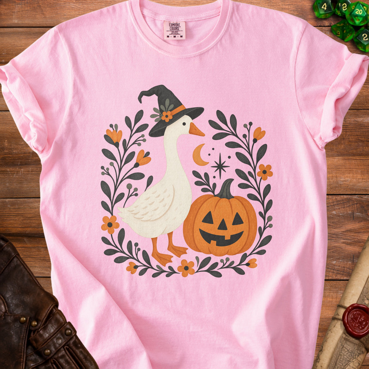 Pink t-shirt with a goose wearing a witch hat and Halloween decor.