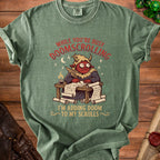 Green t-shirt with a devil character writing on scrolls, reading "While You're Busy Doomscrolling, I'm Adding Doom to My Scrolls."