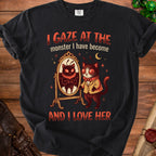 Black t-shirt with a graphic of a cat looking in a mirror at a monster and text.