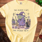 Yellow t-shirt with illustration of witch, black cat, and text "The older I get, the f*cker the n".