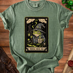 Green t-shirt with tarot card graphic of a tired frog wizard holding a lantern and coffee.
