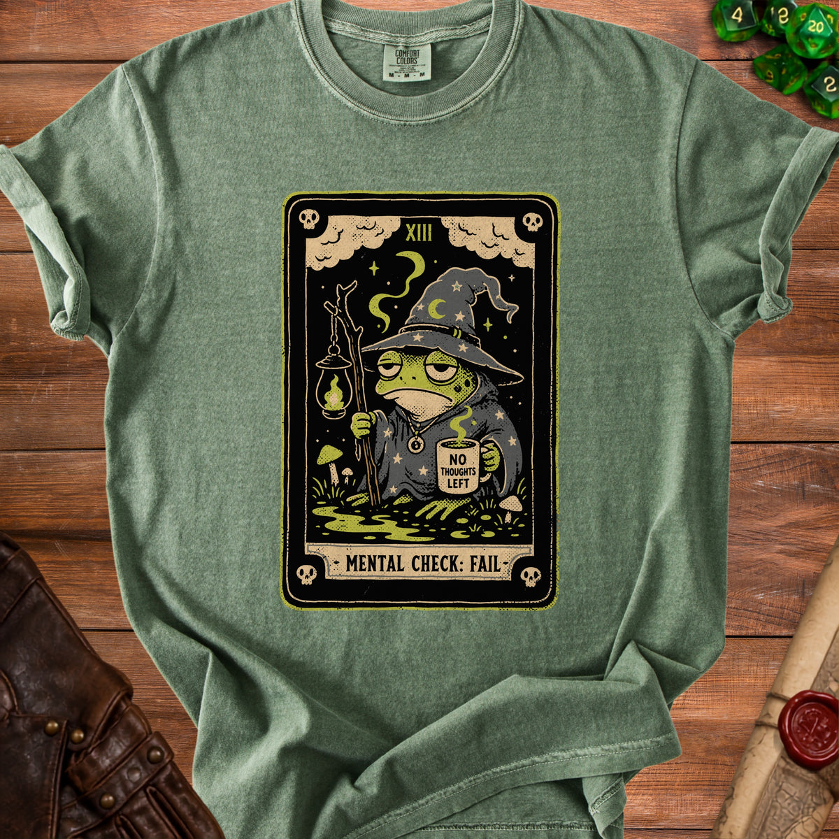 Green t-shirt with tarot card graphic of a tired frog wizard holding a lantern and coffee.